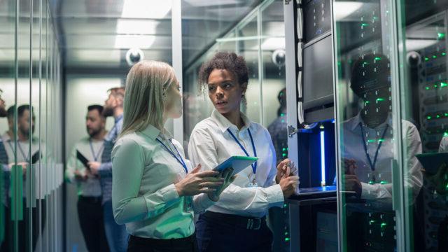 Two women speaking and accessing equipment in a large data center